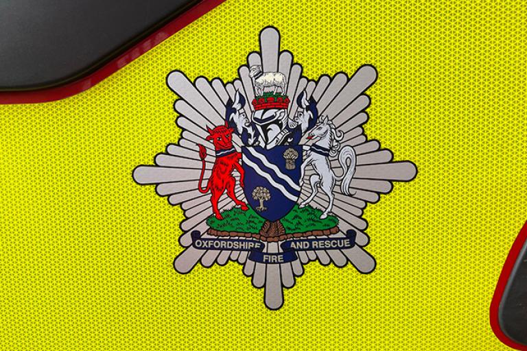 Oxfordshire Fire Service symbol showing a shield, a red Ox and a white horse. Topped with a crown and a sheep.