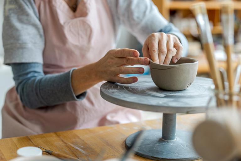 an older woman throwing a pot on a potter's wheel